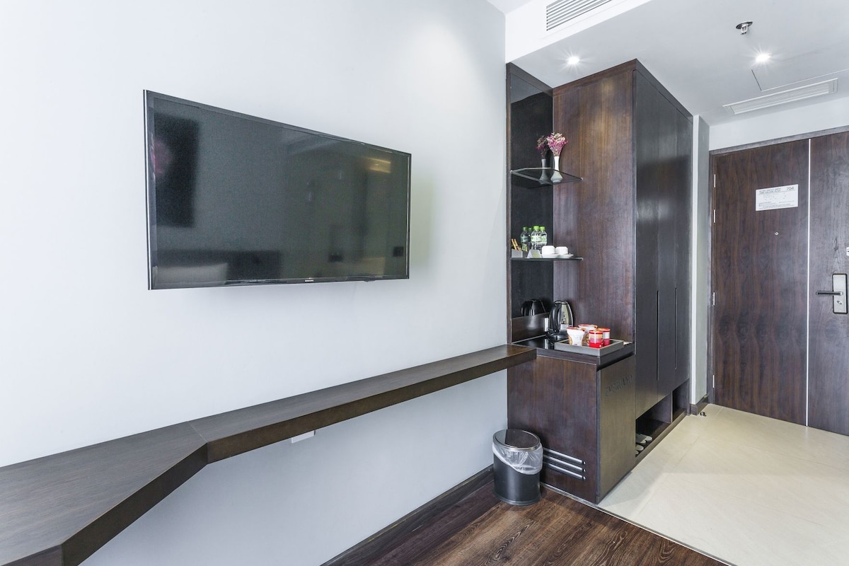 Un pasillo moderno con un televisor de pared, un bote de basura, un estante pequeño con artículos de aseo y un armario de madera oscura.