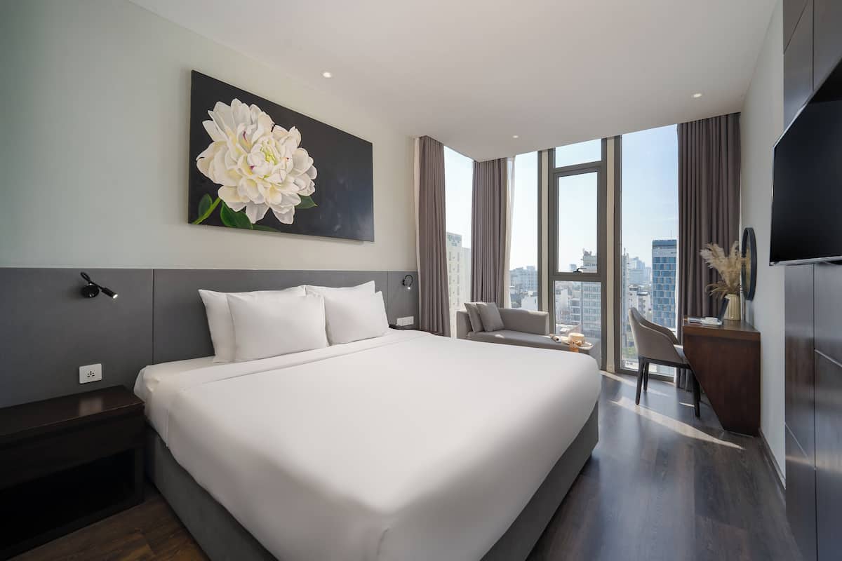 A modern hotel room with a large bed, a seating area with a view of the city, and a flat-screen TV.