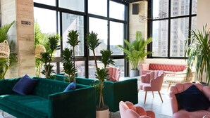 Ein stilvoller Lounge-Bereich mit grün- und pinkfarbenen Polstersitzmöbeln, großen Fenstern mit Blick auf die Stadt und topfpflanzen.