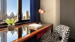 A room with a desk, a lamp, a zebra-patterned chair, a plant, and a view of a cityscape with a tall building.