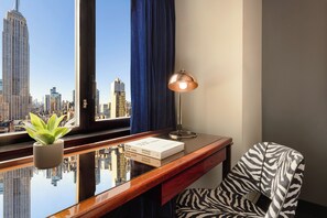 A room with a desk, a lamp, a zebra-patterned chair, a plant, and a view of a cityscape with a tall building.