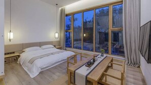 A modern bedroom with a large window, a bed, a bedside table, and a small seating area. - Floral Hotel South Luogu Lane 20 Mansion (Beijing)