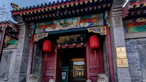 A traditional building with ornate decorations, a red entrance, and two stone lion statues. - Floral Hotel South Luogu Lane 20 Mansion (Beijing)