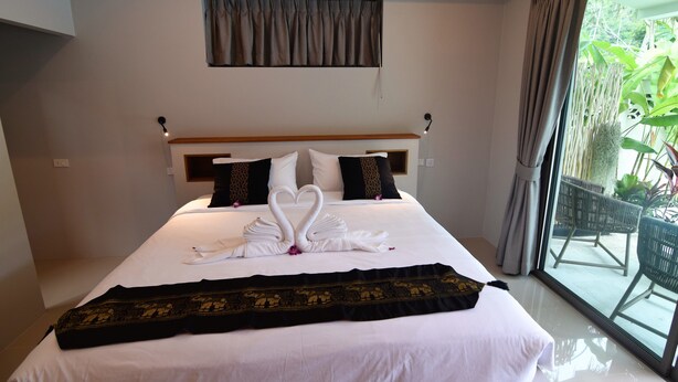 A hotel room with a large bed, a headboard, and a view of the outdoors through a glass door. - Amaya resort (Koh Samui)