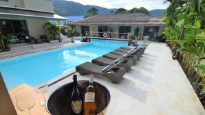A poolside area with lounge chairs, a hot tub, and a table with a bottle of wine and glasses. - Amaya resort (Koh Samui)