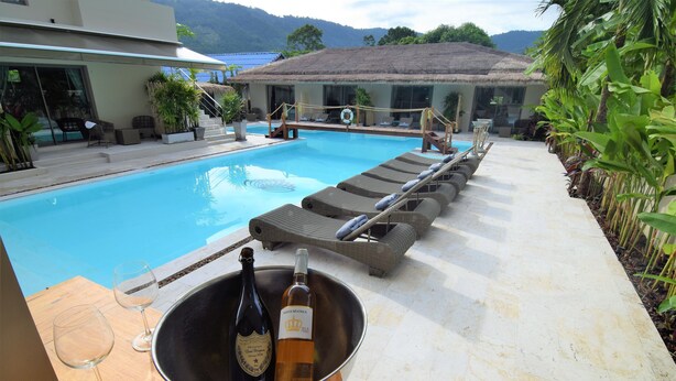 Un área junto a la piscina con sillones de descanso, un jacuzzi y una mesa con una botella de vino y copas.