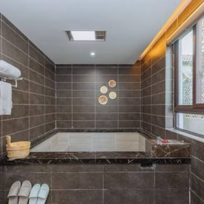 Un baño moderno con baldosas oscuras, una bañera, una ventana y un perchero para toallas.
