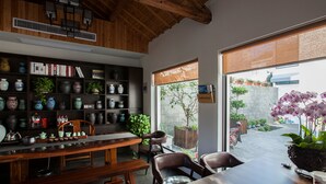 A cozy interior with a wooden ceiling, a bookshelf filled with books and decorative items, a dining area with a table and chairs, and a view of a garden through large windows. - Floral Hotel Nanjing Zuolingyoushe (Nanjing)