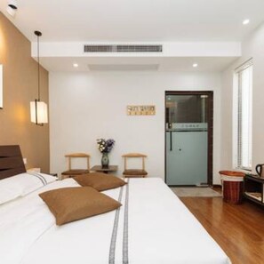 Una habitación de hotel moderna con una cama grande, mesitas de noche, un escritorio pequeño, un refrigerador y una ventana con persianas.
