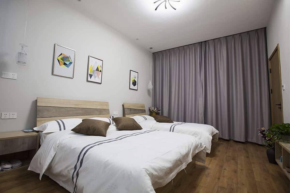Ein modernes Hotelzimmer mit zwei Betten, einem großen Fenster mit grauen Vorhängen und Kunstwerken an den Wänden.