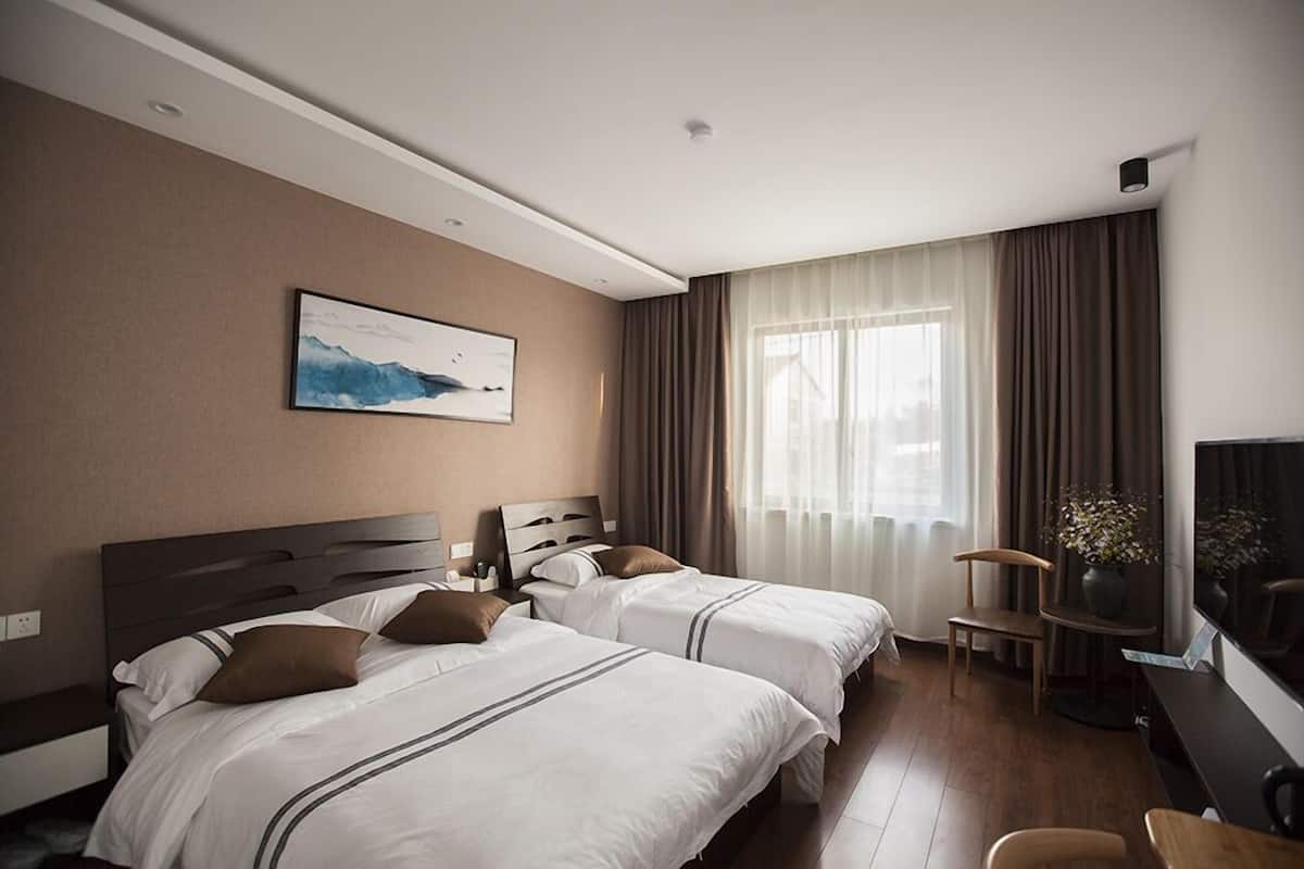 Ein Hotelzimmer mit zwei Betten, einem Schreibtisch, einem Sessel, einem Fernseher und einem Bild an der Wand.