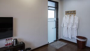 A hotel room with a television, a small table with bottles and a kettle, a door leading to a balcony, and a wall-mounted rack with robes. - Floral Hotel Nanjing Zuolingyoushe (Nanjing)