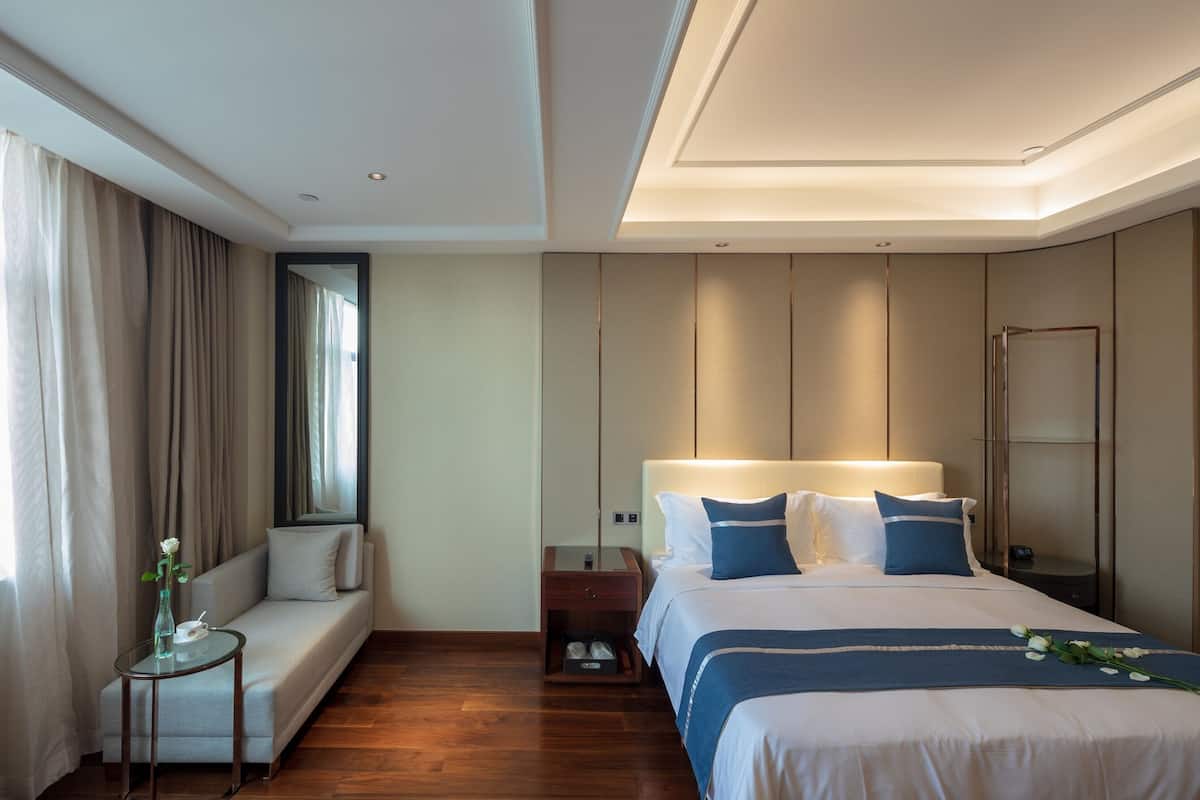 Una habitación de hotel moderna con una cama grande, una mesita de noche, un sofá y una ventana con cortinas.
