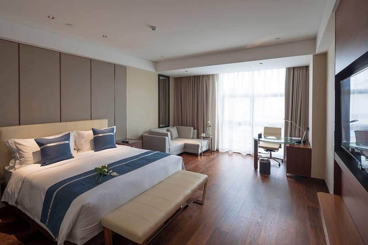 Una habitación de hotel moderna con una cama grande, una zona de estar con sofá y sillones, una mesita y un ventanal con vistas.