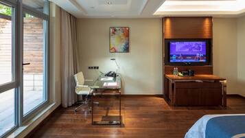 A hotel room with a large window, a desk with a chair, a television, and a bed.