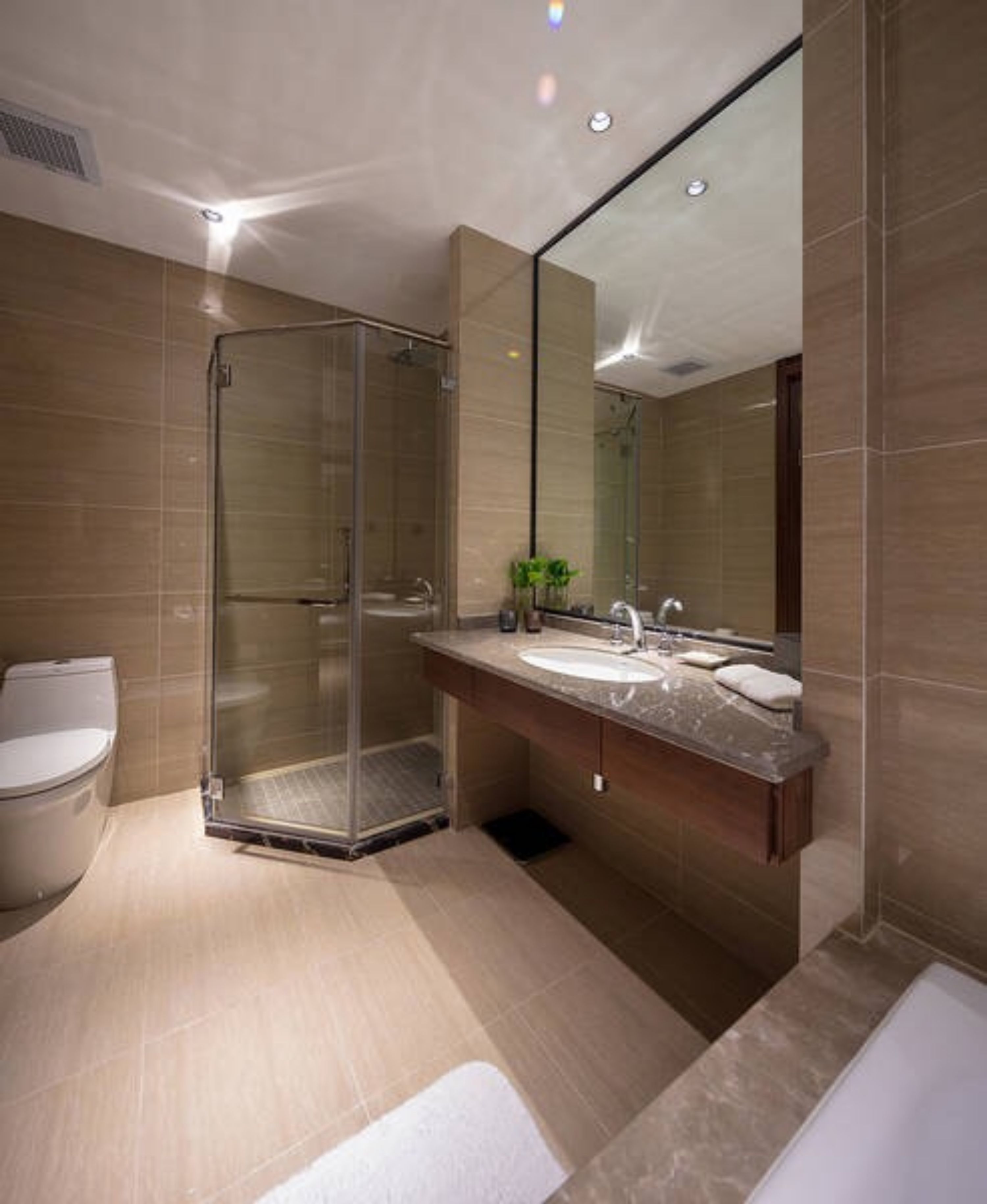 A modern bathroom with a glass-enclosed shower, a large mirror, and a marble countertop.