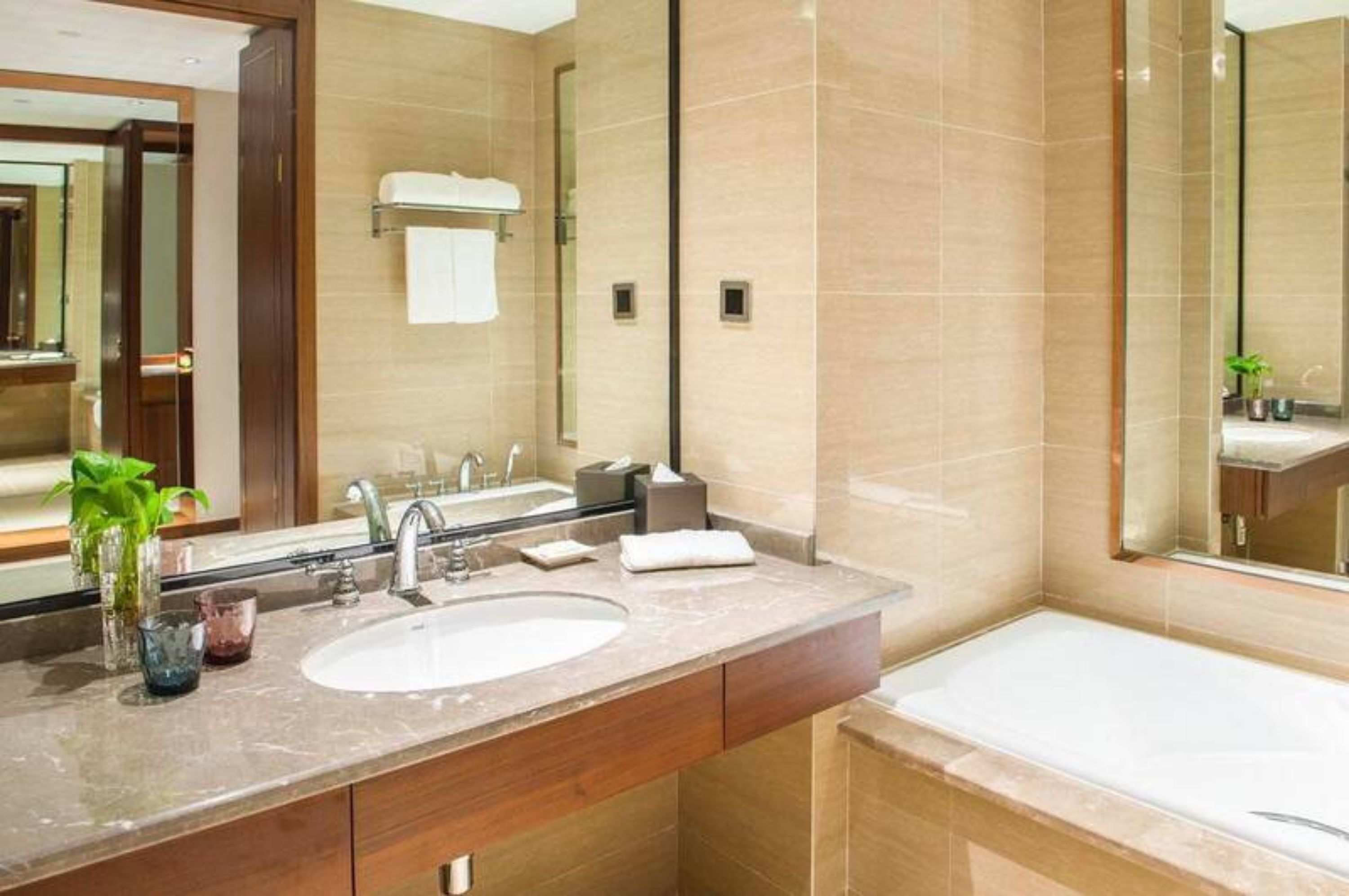 A modern bathroom with a large mirror, two sinks, a bathtub, and a wooden vanity.