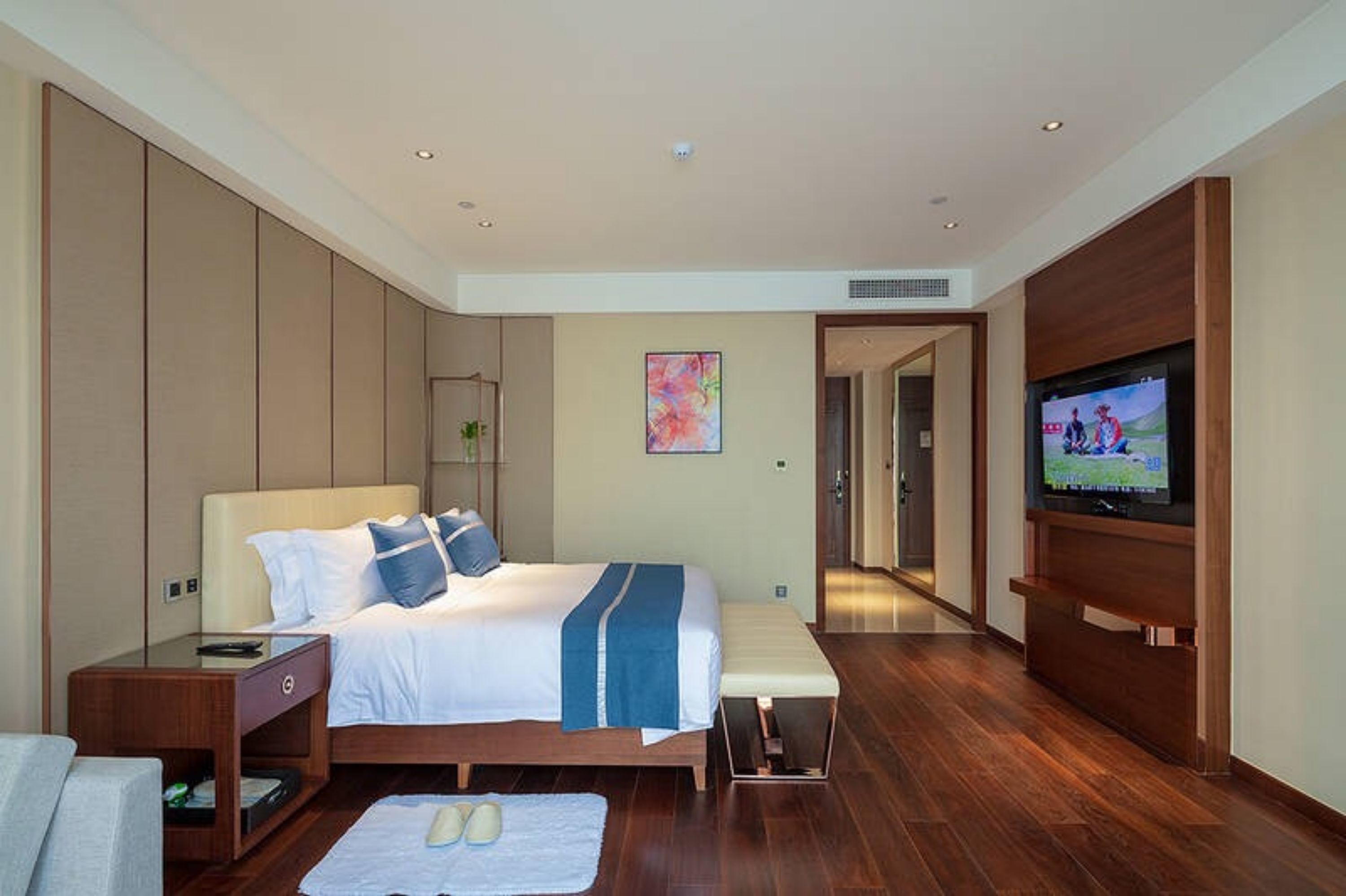 A modern hotel room with a large bed, a TV, and a wooden floor.