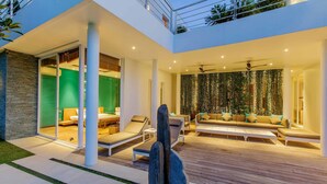 A modern outdoor living area with a wooden deck, lounge chairs, and a seating area with sofas and cushions. - Phocea Golf View Villa by Premier Hospitality Asia (Pecatu)