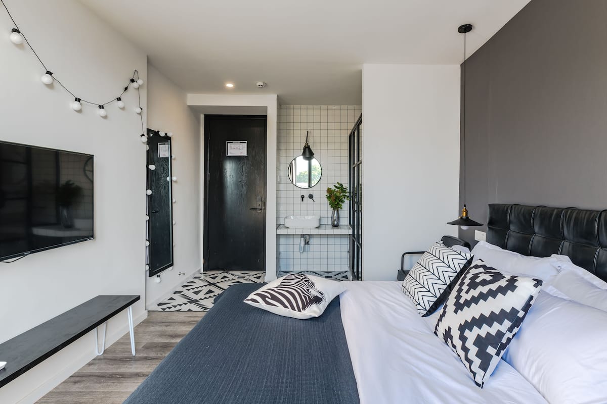 Ein modernes Schlafzimmer mit einem großen Bett, einer Bank, einem Fernseher, einem Spiegel und einem durch eine offene Tür einsehbaren Badezimmer.