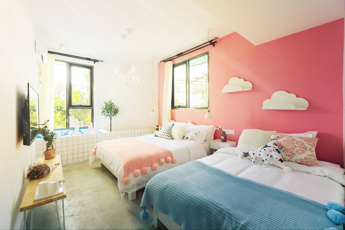 Ein Schlafzimmer mit zwei Betten, einem kleinen Tisch mit Pflanze und einem Fenster mit Blick auf Grünflächen.