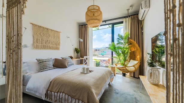 A modern bedroom with a bed, bedside table, hanging macrame decor, and a view of greenery outside. - Floral Hotel Xiamen Menglou (Xiamen)