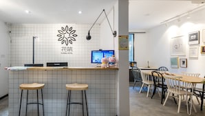 A hotel reception area with a tiled wall, a reception desk, two bar stools, a computer monitor, and a dining area with chairs and a table. - Floral Hotel Xiamen Menglou (Xiamen)
