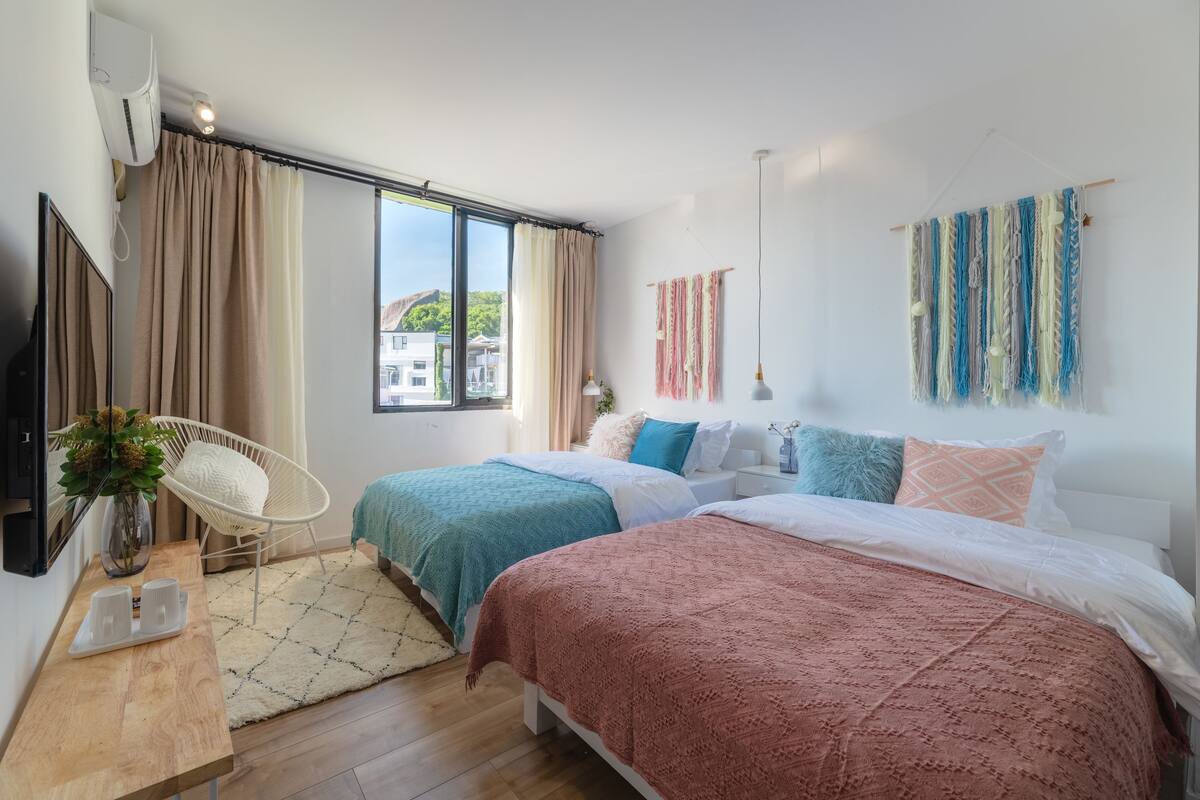 Ein modernes Schlafzimmer mit zwei Betten, einem großen Fenster und Blick auf Gebäude.