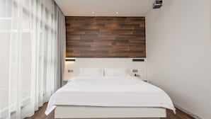 A modern bedroom with a wooden headboard, a large bed, white bedding, and a nightstand with a lamp. - Floral Hotel Xiamen Buxiang Inn (Xiamen)