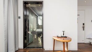 A modern hotel room with a wooden floor, a glass door leading to a bathroom, and a small wooden table with a kettle. - Floral Hotel Xiamen Buxiang Inn (Xiamen)
