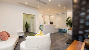 A modern reception area with a white reception desk, a seating area with a white sofa and a white armchair, and a large potted plant. - Floral Hotel Xiamen Buxiang Inn (Xiamen)