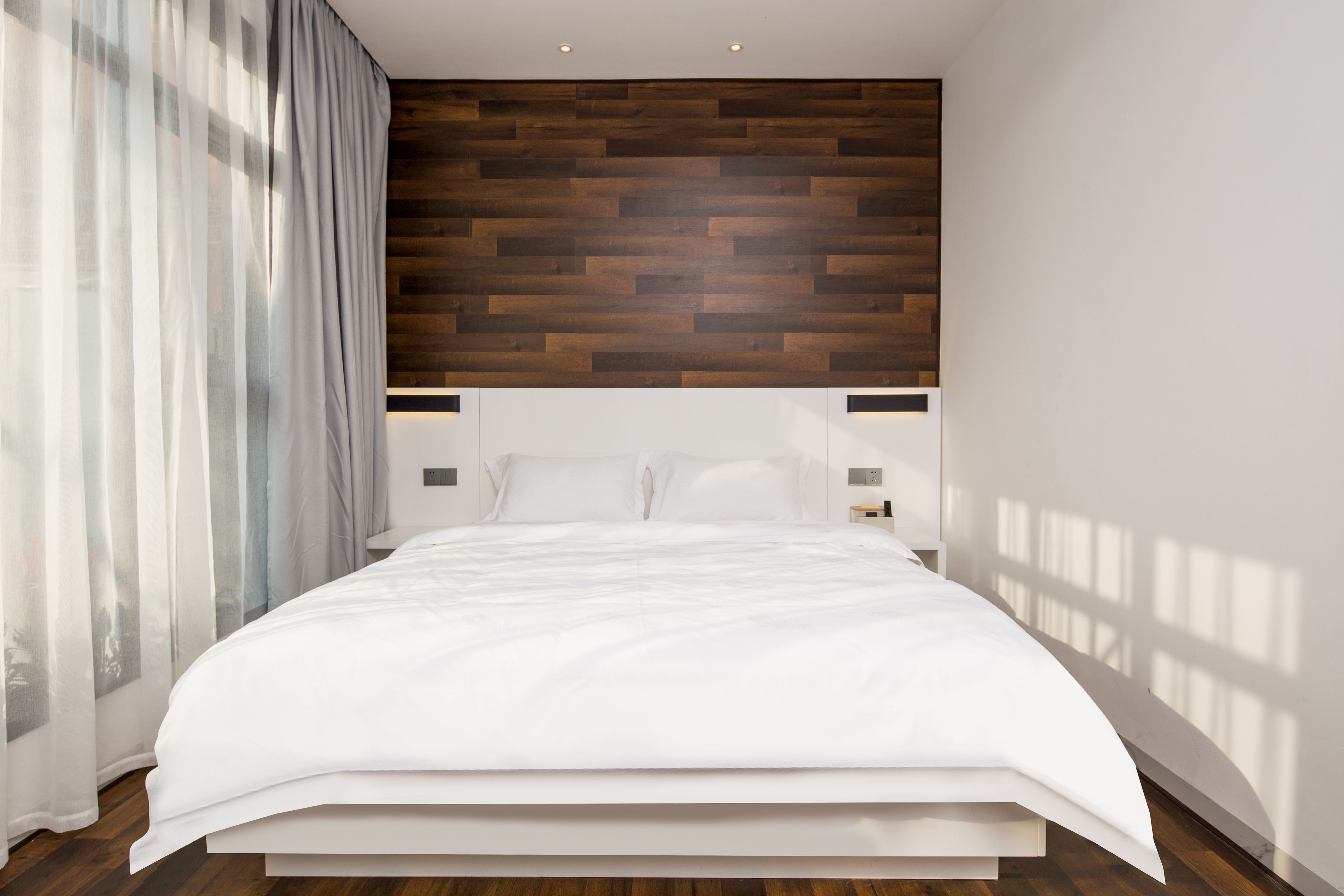 Un dormitorio moderno con cabecera de madera, una cama grande y una mesita de noche.