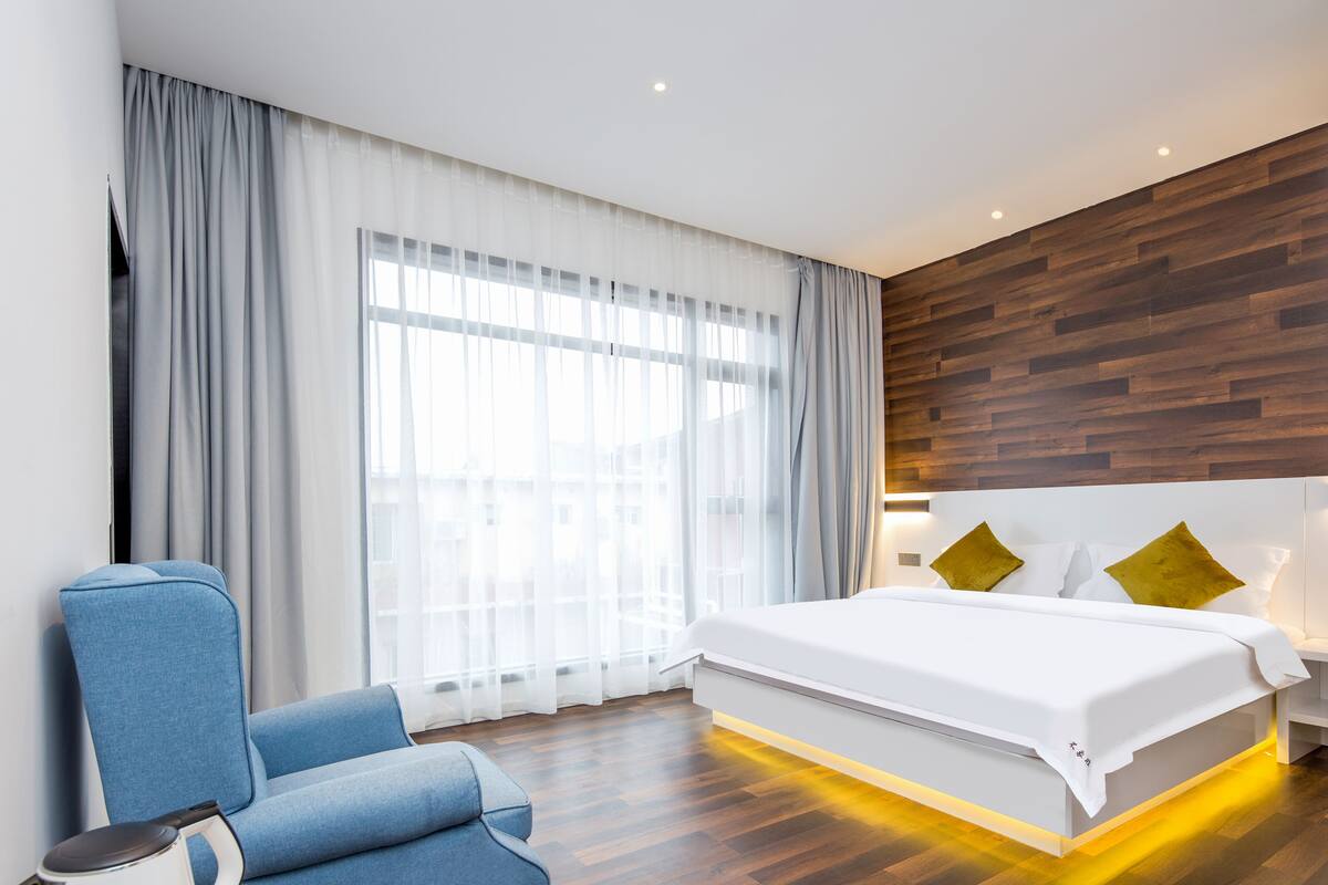 A modern hotel room with a large bed, a blue armchair, and a wooden accent wall.