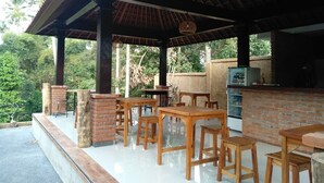 An outdoor patio with wooden tables and chairs, a brick fireplace, and a grill area.