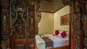 An ornate wooden door with intricate carvings, a bed with a white mattress and red pillows, and a framed artwork on the wall.