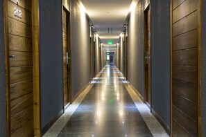 Un couloir d’hôtel avec des portes en bois, un sol en marbre et un panneau de signalisation de sortie vert.