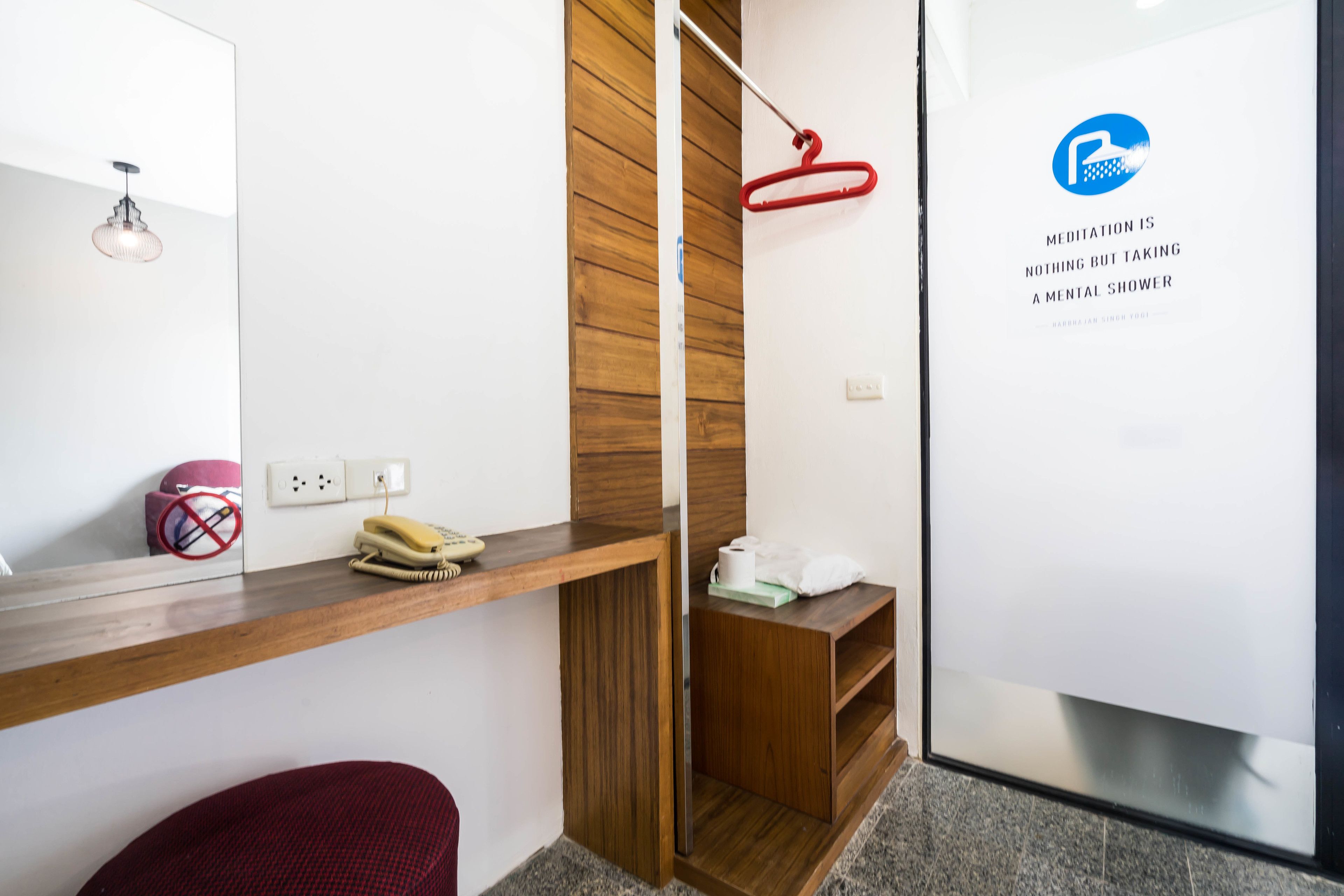 A modern bathroom with a wooden vanity, a red towel rack, a mirror, and a wall-mounted sign with a meditation quote.