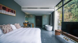 A modern hotel room with a large bed, a desk, a bathtub, and a TV.