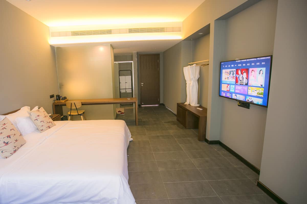 A hotel room with a bed, a desk, a chair, a TV, and a bathroom visible through an open door.
