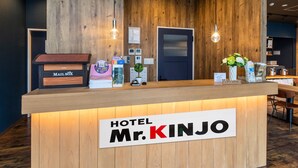 Un mostrador de recepción de hotel con detalles de madera, un letrero que dice "HOTEL Mr. KINJO" y un buzón de correo etiquetado "MAIL BOX".