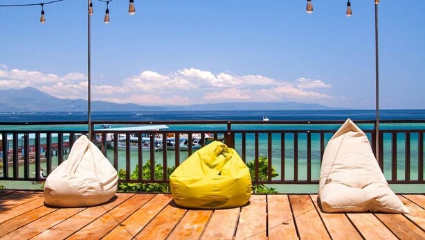 Eine Holzterrasse mit drei Sitzsäcken, Lichterketten und Blick auf das Meer und die Berge.