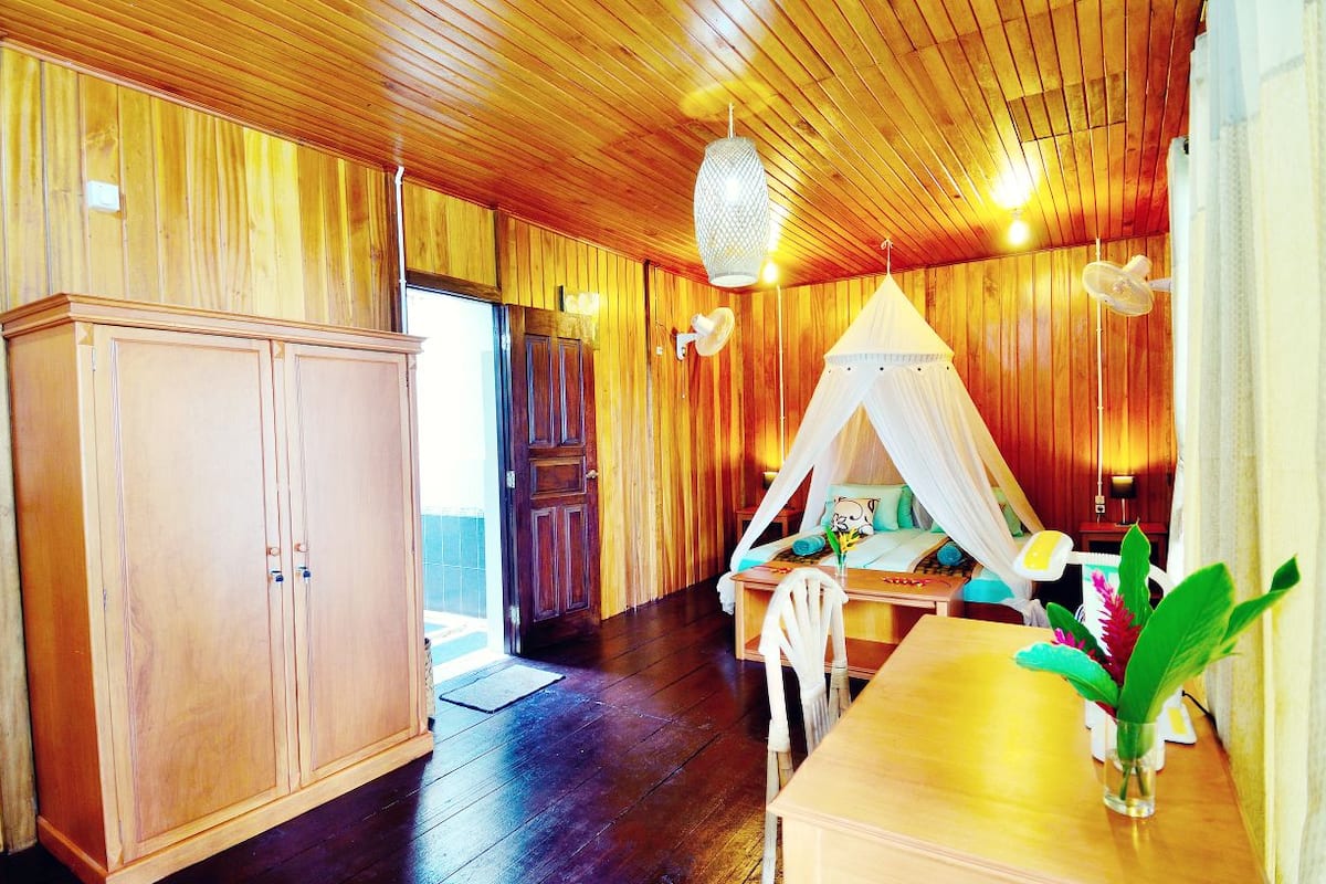 A wooden interior with a large cabinet, a tent-style bed, and a dining area.