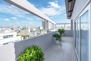 A balcony with potted plants, a city view, and a modern building facade.