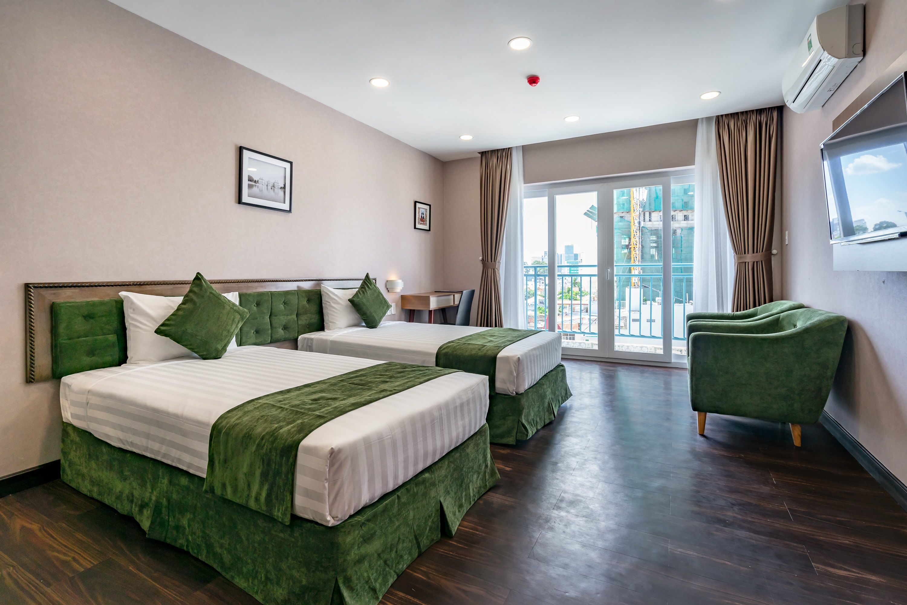 Une chambre d’hôtel avec deux lits, un fauteuil vert, un balcon avec vue et un téléviseur fixé au mur.