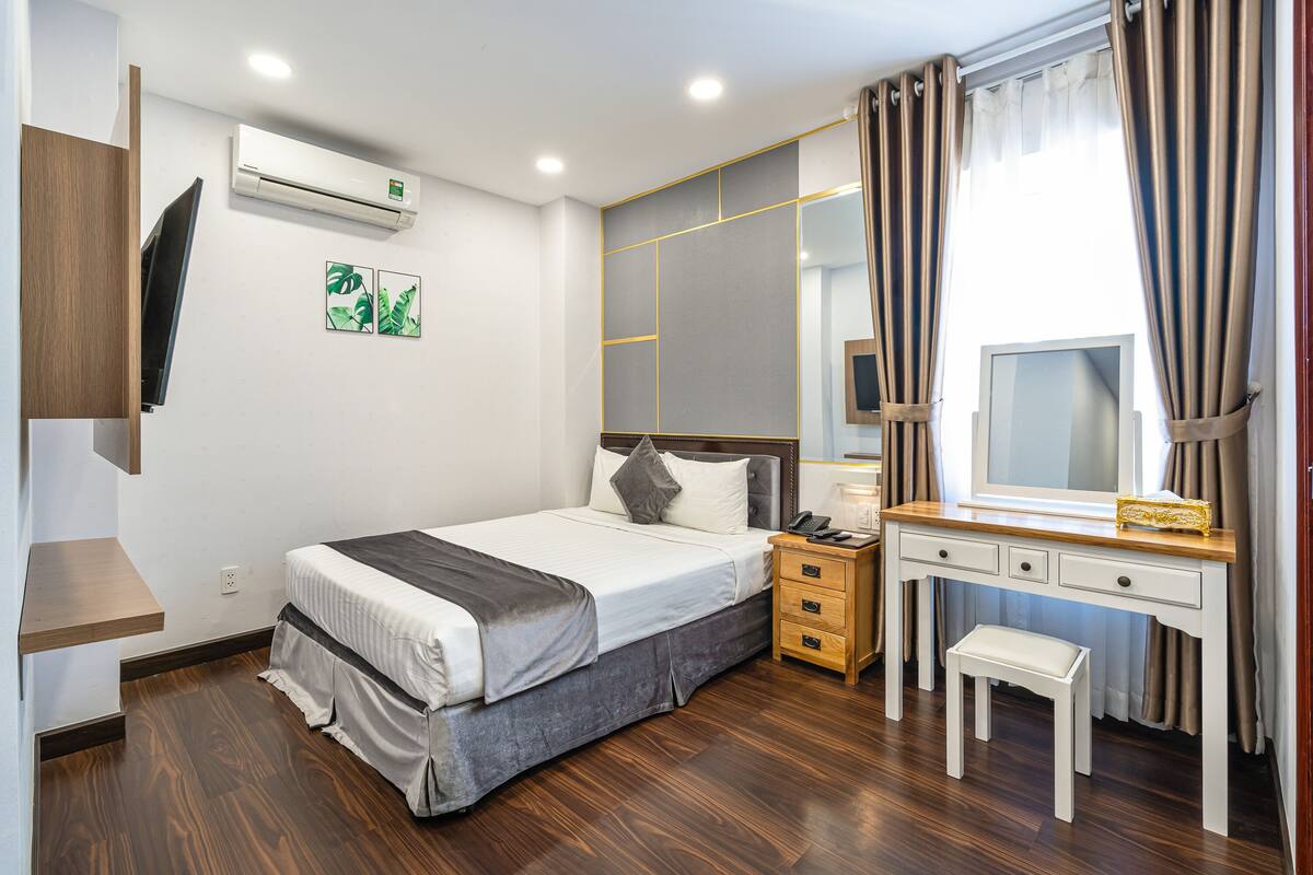 Quarto com cama, mesa de cabeceira, espelho e escrivaninha com cadeira.