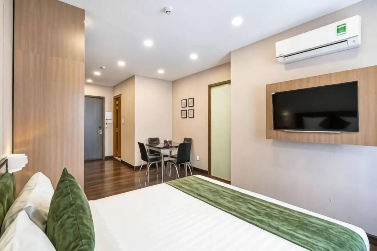 Quarto de hotel com uma cama, televisão fixada na parede, mesa de jantar com cadeiras e ar condicionado.