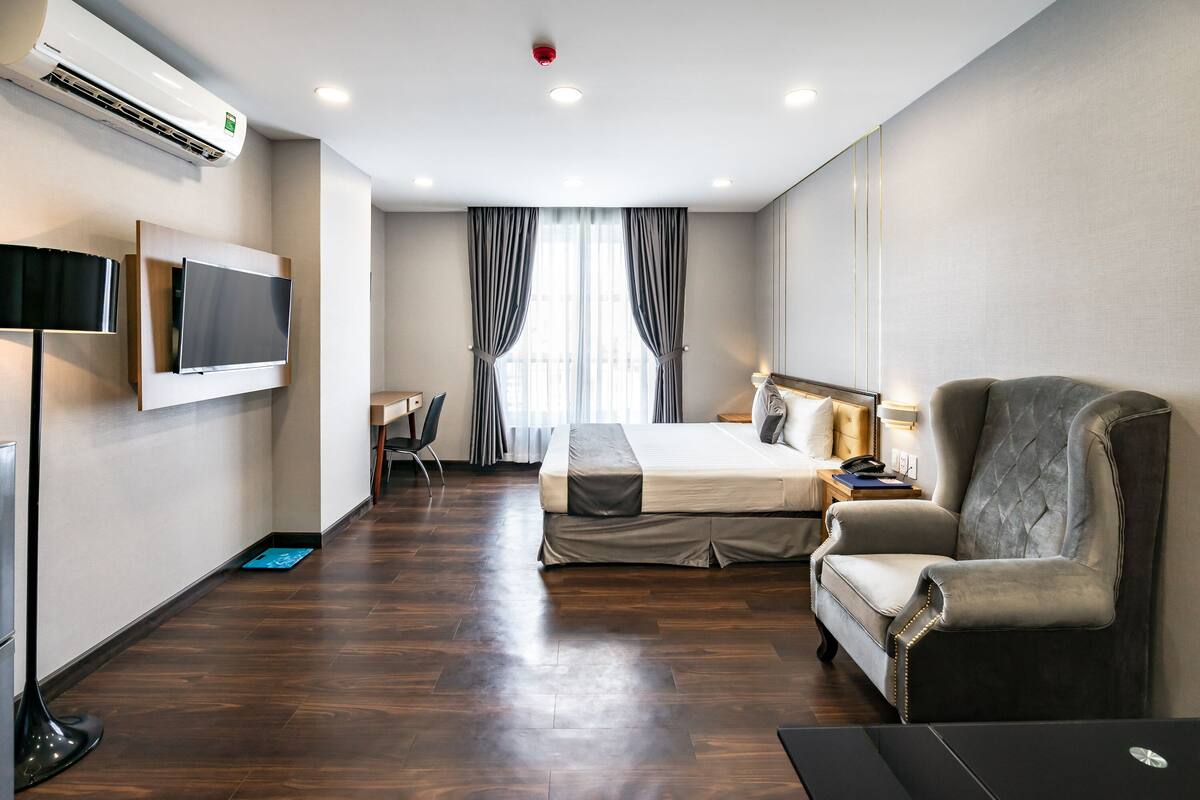 Quarto de hotel com cama, escrivaninha, cadeira, televisão e aparelho de ar condicionado.