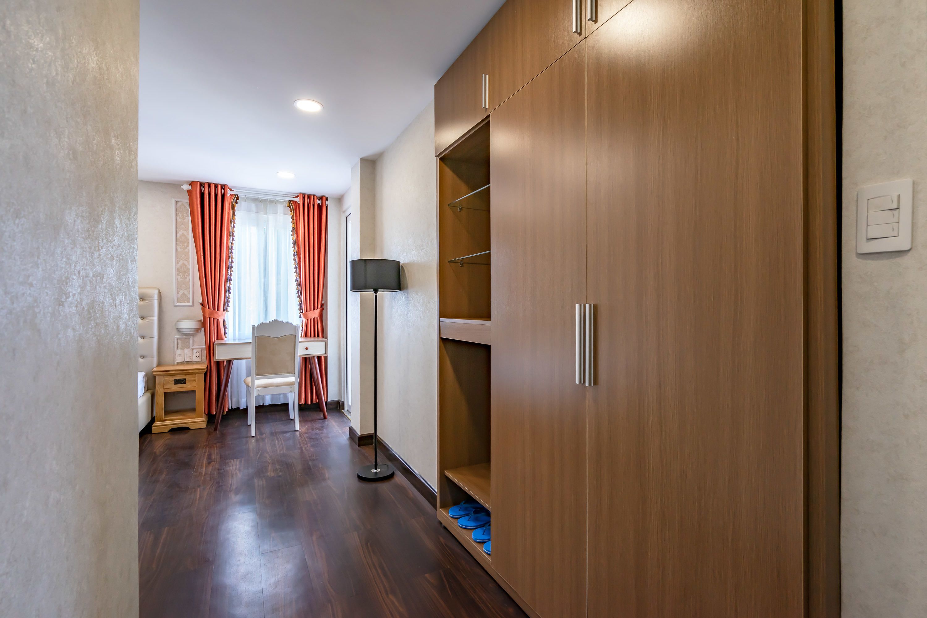 Un couloir avec une armoire en bois, une petite table avec une lampe et une chaise.