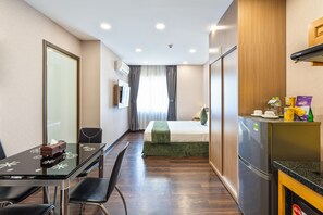 A compact hotel room with a bed, a small kitchenette, a dining table with chairs, and a large window with curtains.