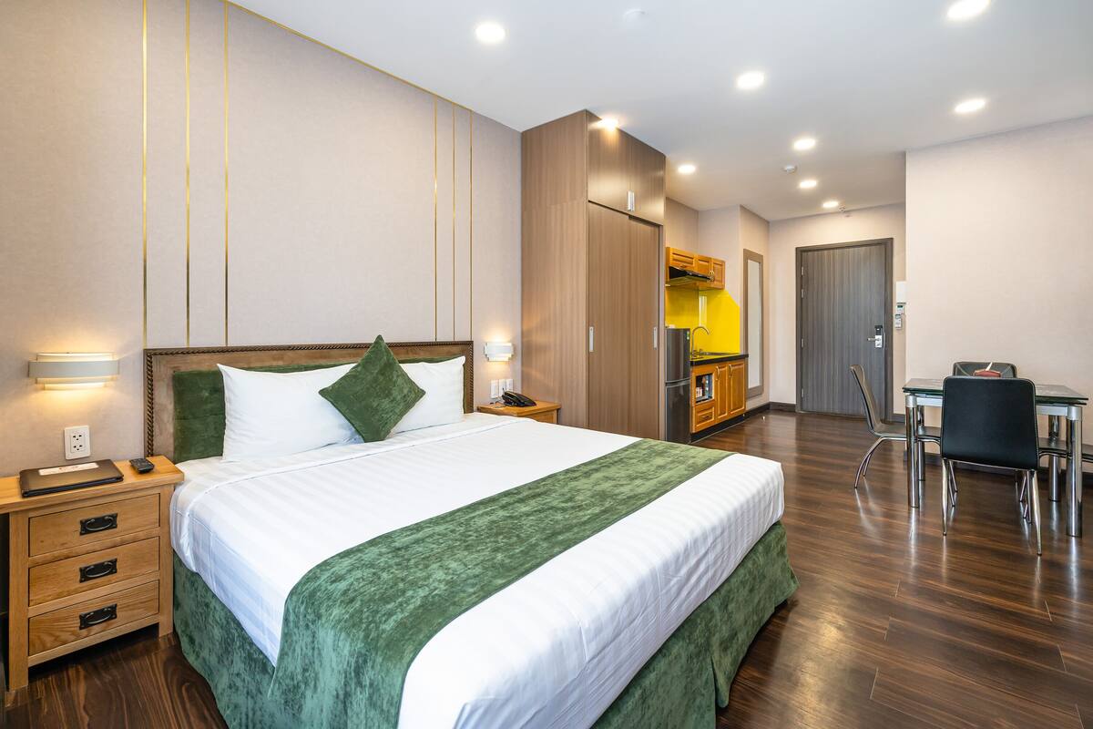 Quarto de hotel com uma cama grande, uma escrivaninha, uma cadeira, um guarda-roupa e uma kitchenette.